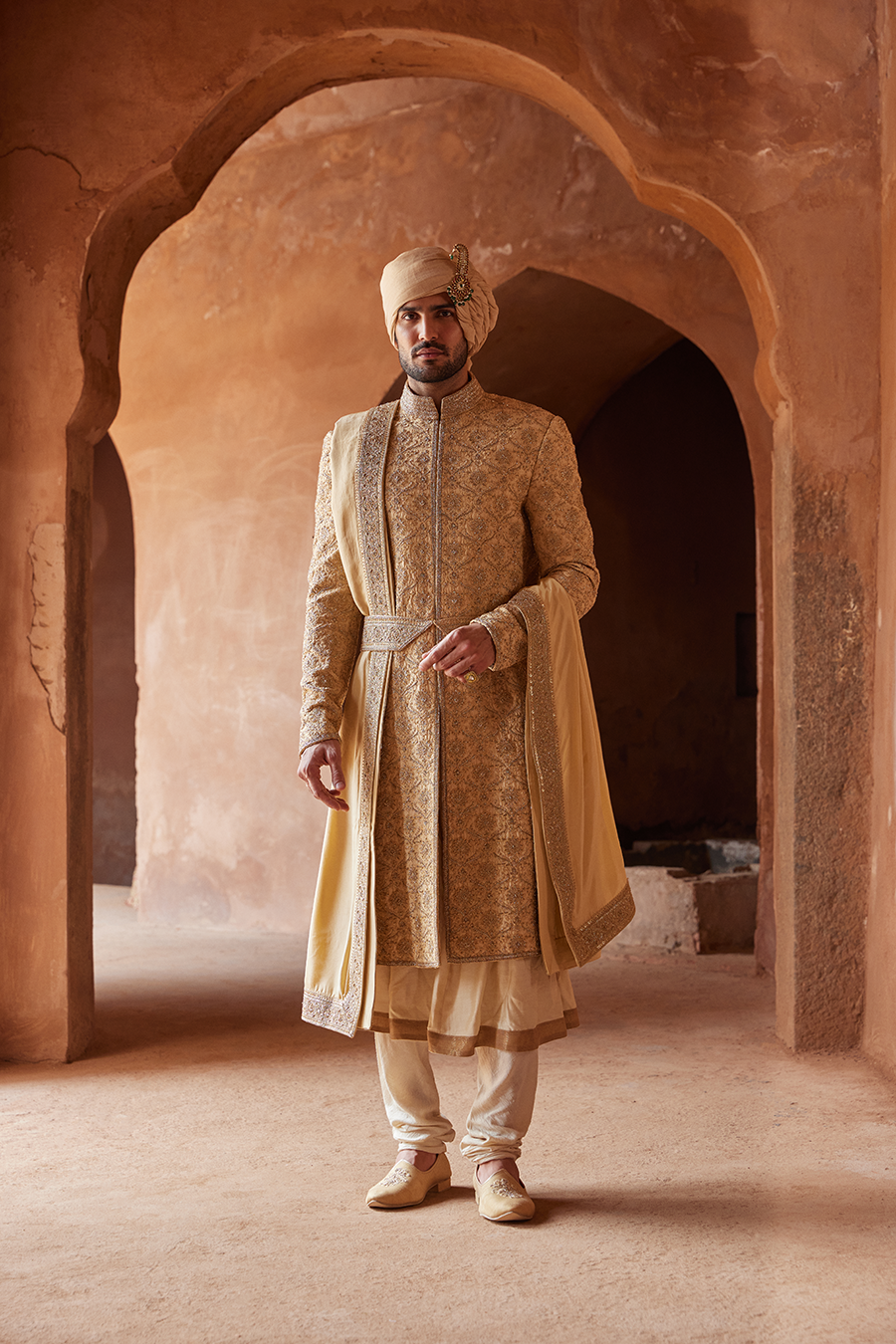 GOLD RAW SILK SHERWANI WITH KURTA AND CHURIDAR WITH AN OPTIONAL WORKED BELT, STOLE AND JUTIS.